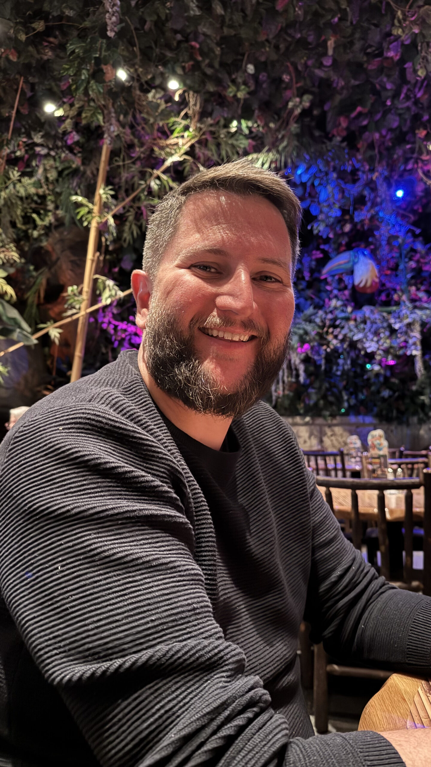 Homem sorrindo dentro do Rainforest Cafe com ambiente de selva e iluminação ao fundo