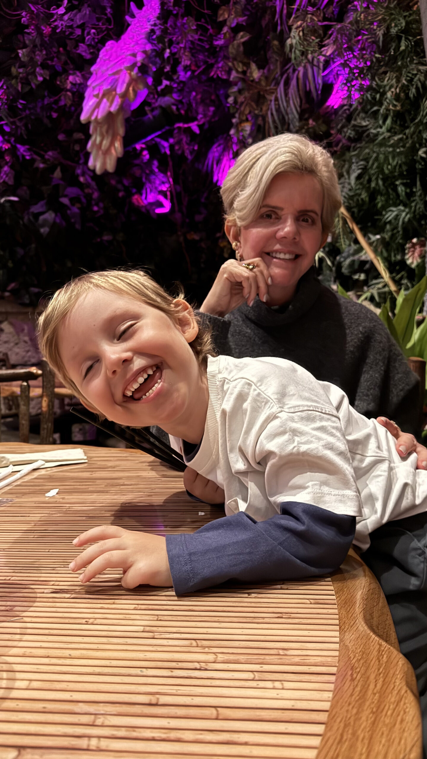 Criança rindo com a avó dentro do Rainforest Cafe com ambiente iluminado em roxo ao fundo