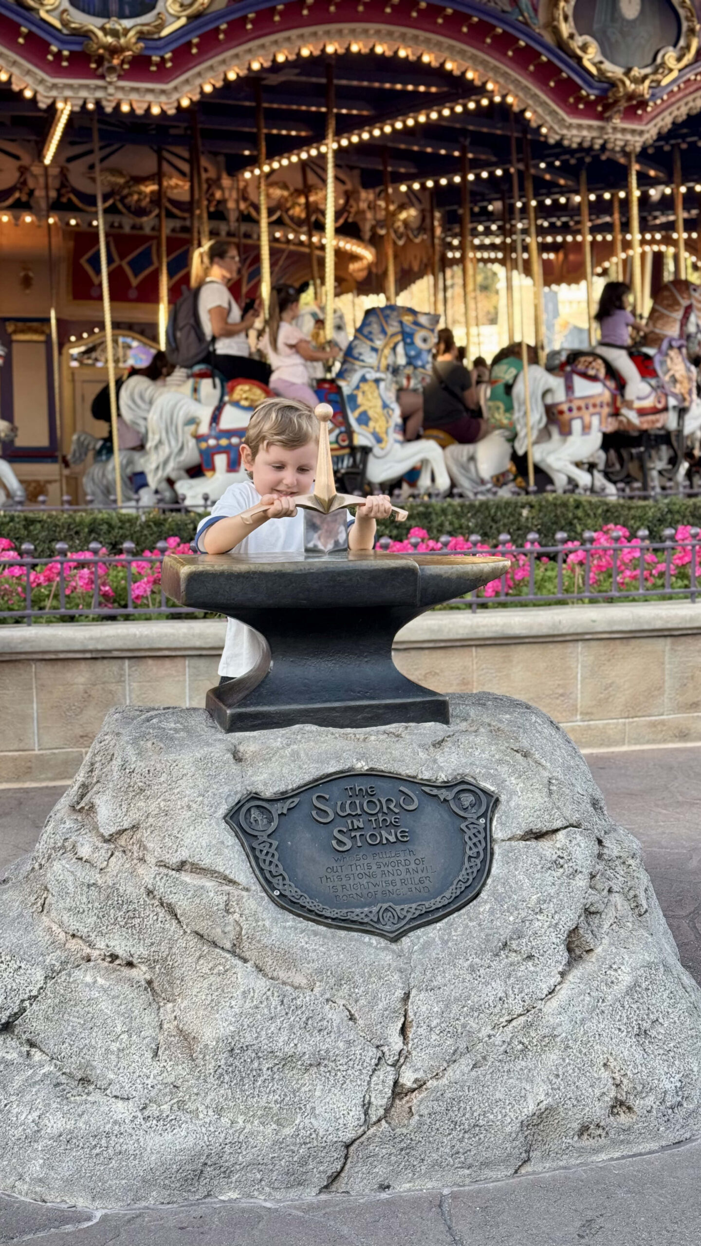 Samuel tentando puxar a espada na pedra em frente ao carrossel do Magic Kingdom