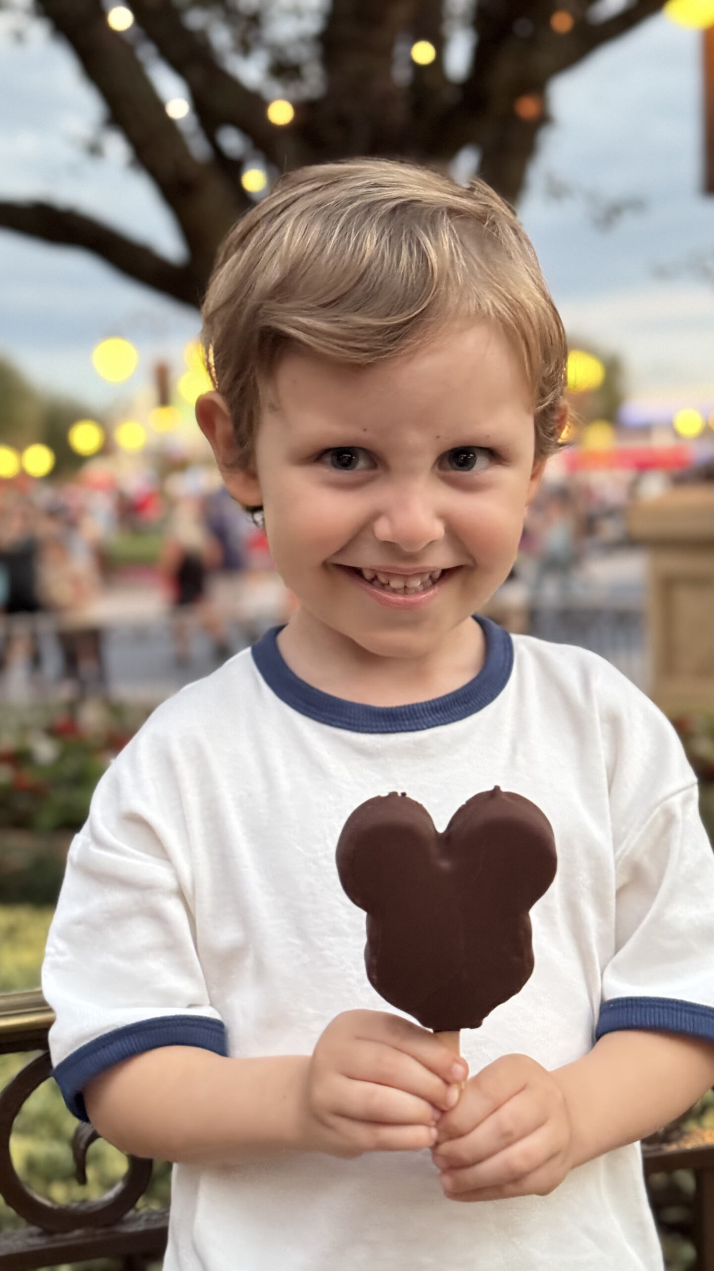 Samuel sorrindo com o picolé do Mickey no Magic Kingdom ao entardecer
